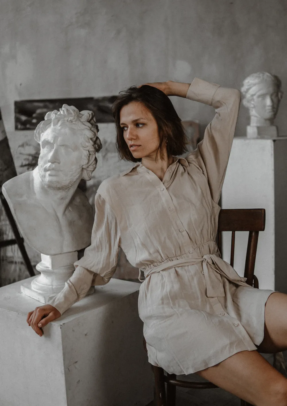 A woman seated beside classical marble busts in an Athens studio