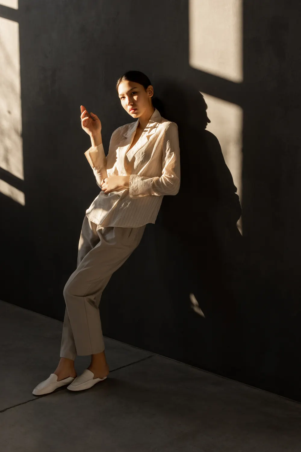 A woman in warm neutral tailoring in hard afternoon light